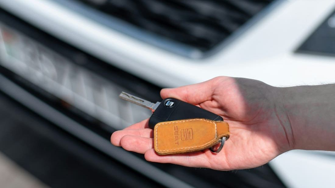 Car key held out in front of the grille of a white used vehicle